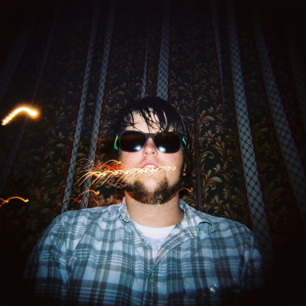 man with sunglasses sitting in front of a curtain and light flares on the picture