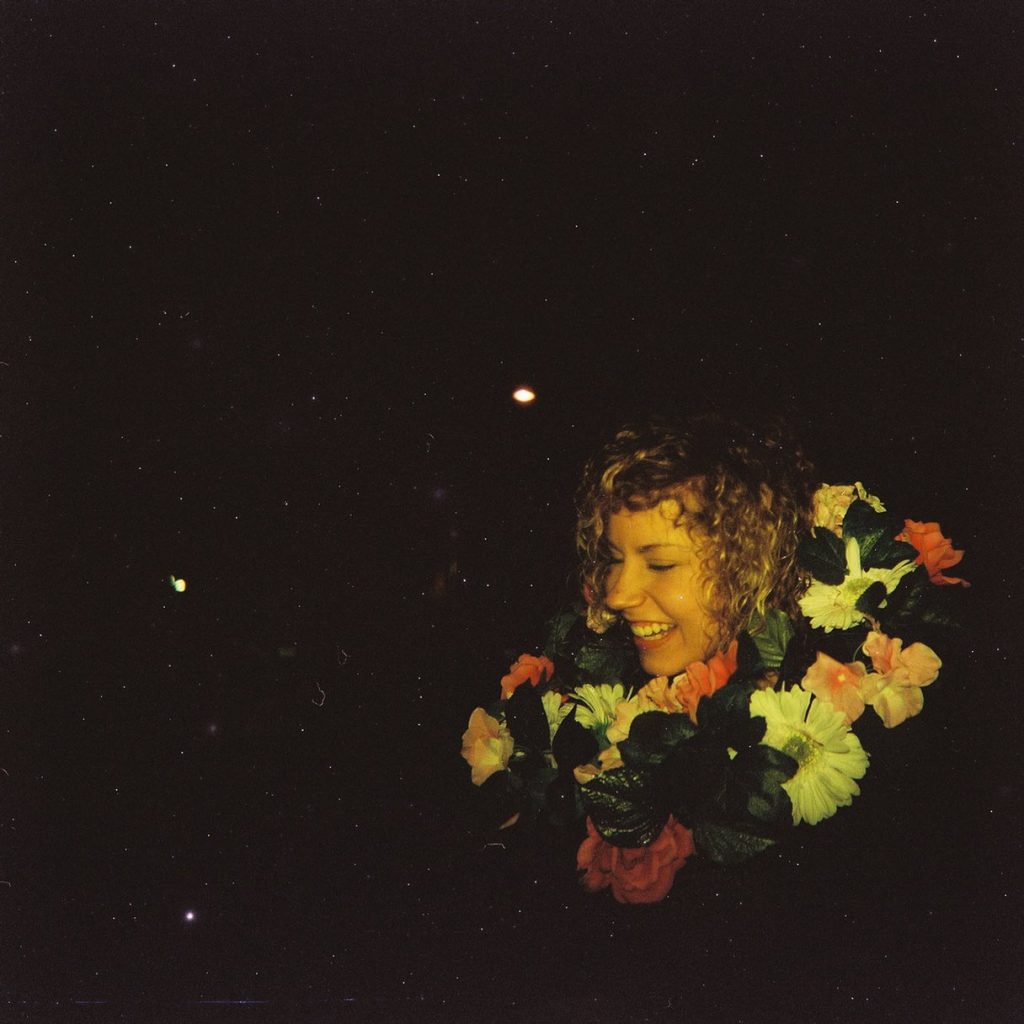 a laughing woman at night with flowers around her neck